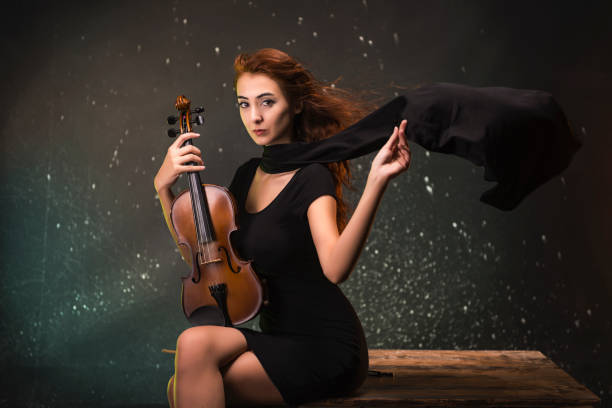 istock Beautiful young woman playing violin over black background. 1328567716