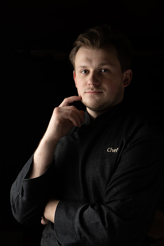 Portrait of a young cook сhef in a jacket on a dark background