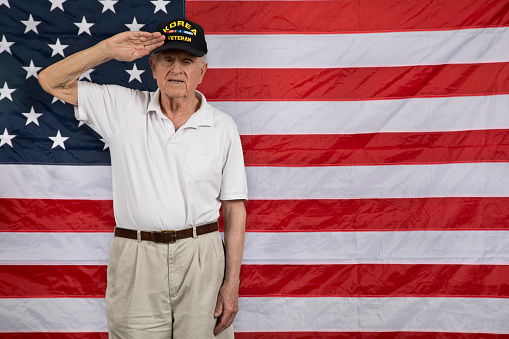 War Veteran standing proudly in front of national flag.