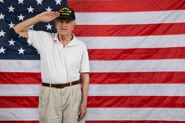 veterano de guerra coreano em pé na frente da bandeira americana olhando para a saudação da câmera - korean war - fotografias e filmes do acervo