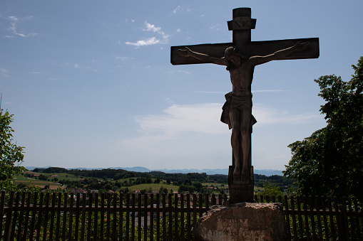 Andechs, Starnberg, Germany - July 12, 2021: A crucifix on the grounds of the Andechs Monastery, an important pilgrimage site in Upper Bavaria, with a view of the surrounding area, in summer.
