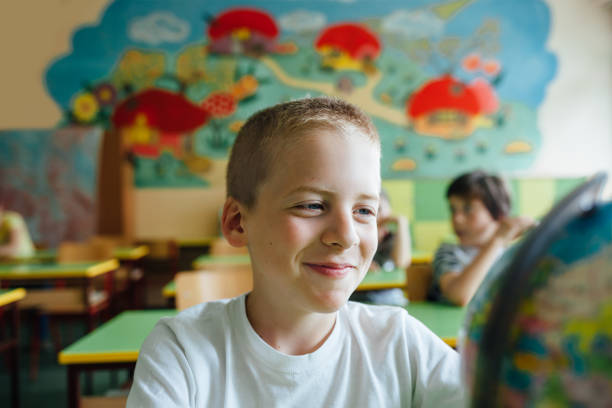 Happy boy looks at a globe in a classroom.