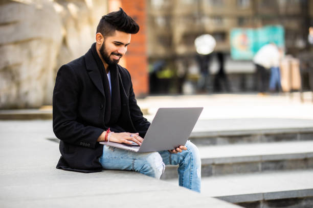 istock Handsome young indian manager working on laptop while sitting outdoors on the stairs. 1328578287