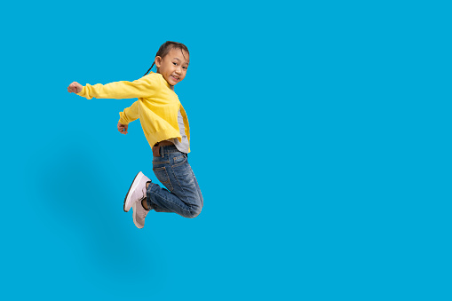 Funny asian child girl jumping on a colored Blue background