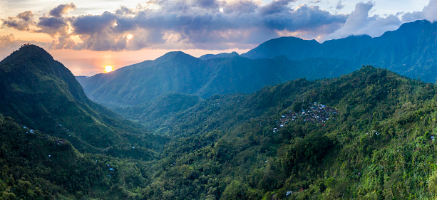 Aerial panoramic landscape of the mountain range in Bali with the sun rising over the ocean and illuminating the valley.