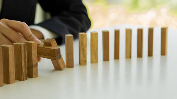 A businessman protects a falling wooden block on a row of tables. A businessman protects a falling wooden block on a row of tables. recession protection stock pictures, royalty-free photos & images