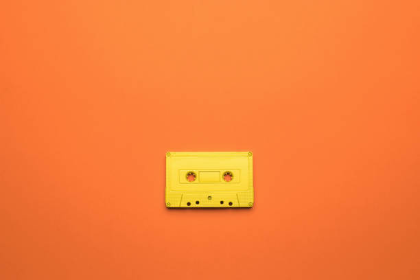 istock A bright yellow cassette with a magnetic tape on an orange background. Flat lay. 1328599992