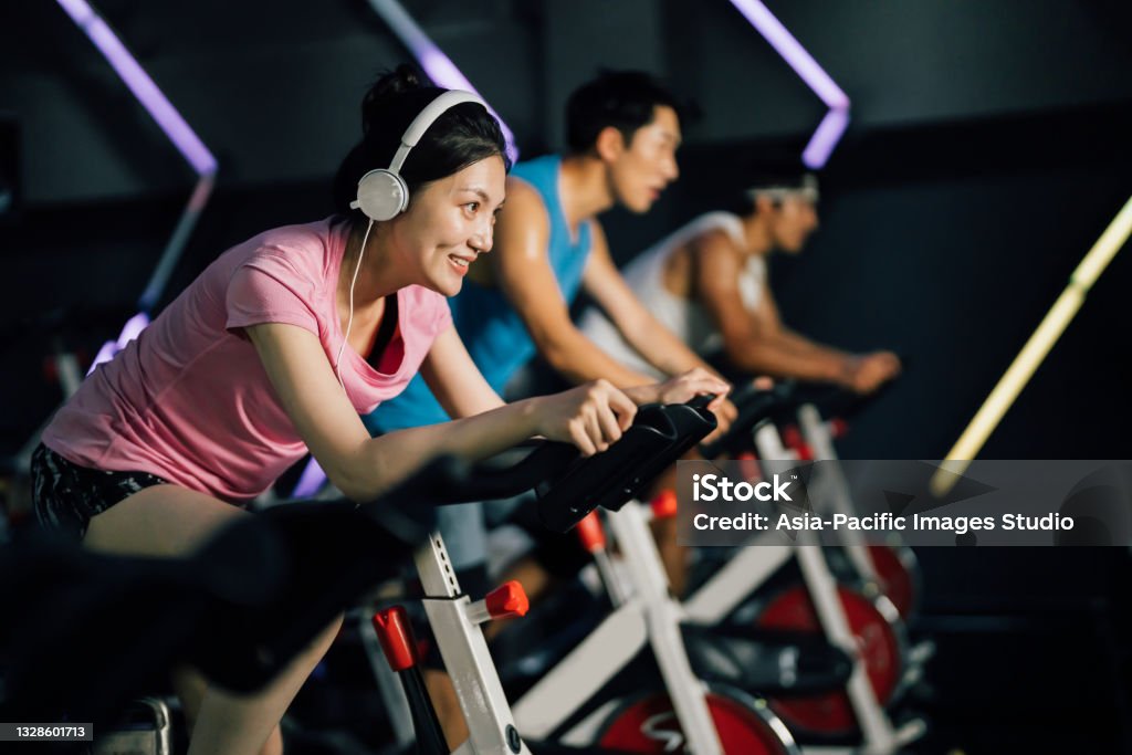 Asian young woman riding stationary bike at gym. Health and fitness concept. Asian young woman cycling on an exercise bike at gym. Stationary Cycling Class Stock Photo