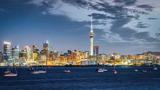 New Zealand Auckland Skyline - Cityscape Panorama. Iconic illuminated Sky Tower of Auckland and cityscape of downtown Auckland in sunset twilight. Yachts, tourboats and motorboats anchored in the Auckland harbour bay.  Auckland, New Zealand, Oceania