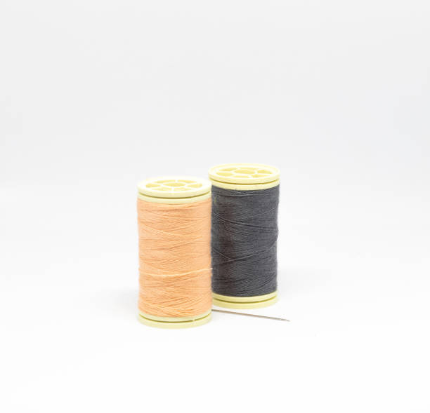 istock Spools of two contrast colors (cream and blue) thread on isolated white background with a sewing needle in the middle 1328611009