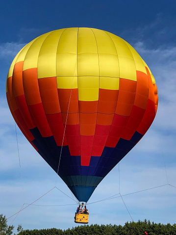This beautiful colorful hot air balloon is tethered for rides at the first annual Taste N Glow Festival in Wausau, Wisconsin on July 10, 2021.  The vivid blue sky has white clouds.