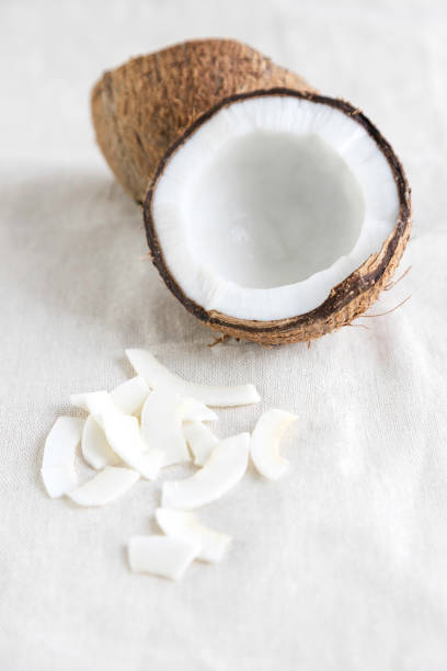 virutas de coco en un mantel de lino y la mitad de un coco fresco cerca. un snack saludable ideal para nutricionistas, veganos y vegetarianos. - coconut flakes fotografías e imágenes de stock