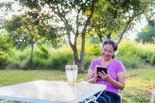 Happy Asian women using digital tablets and listening to music sitting in the park at outdoors, People lifestyle relaxing and technology concept