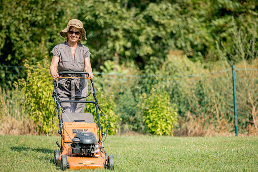 Senior woman mowing grass. Old woman gardening and mowing the grass with a lawn mower in the garden