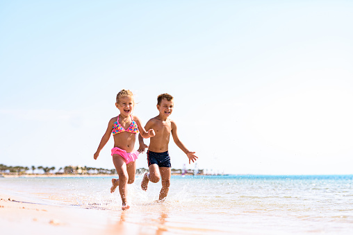 Carefree siblings having fun while running during summer day on the beach. Copy space.