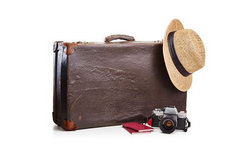 Old fashioned vintage brown leather suitcase with a film camera, a straw hat and two passports on white. Ready for travel and holiday concept