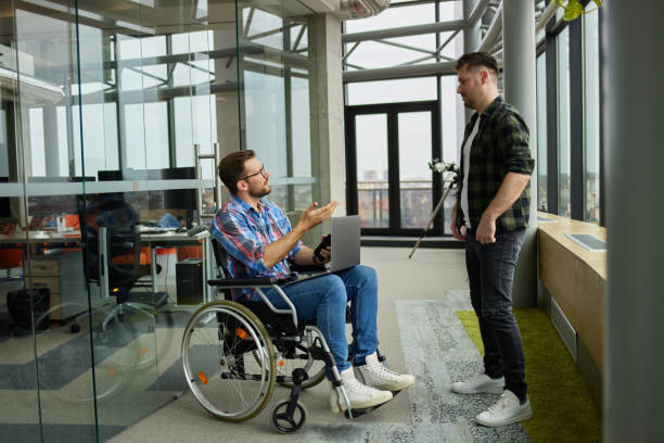istock Disabled computer programmer discussing with male coworker in office hallway 1328627523