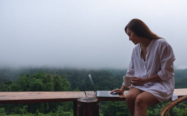 istock A woman using and working on laptop computer while sitting on balcony with a beautiful nature view on foggy day 1328628911