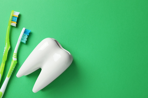 Toothbrushes and holder on green background, flat lay. Space for text