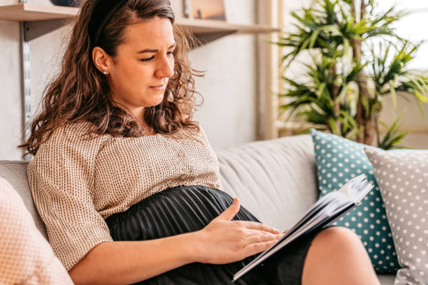 istock Pregnant woman sitting on sofa and reading book 1328630059