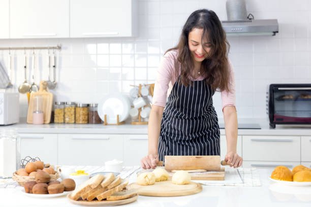 smiling young woman work with wooden roller pin making sweet pie or pastry dough in kitchen, happy millennial female loving wife cooking in apron preparing family dinner or dessert baking buns - cake making mixing eggs imagens e fotografias de stock