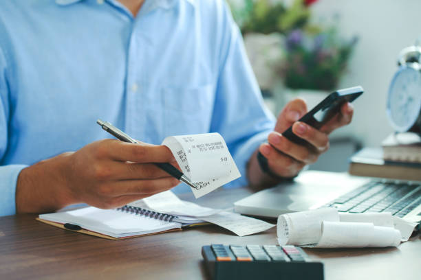 スマートフォンを使用し、ホームオフィスでコストをチェックする手形を保持している男、ファイナンス.税制を数え始めます。 - tax tax form refund financial advisor ストックフォトと画像