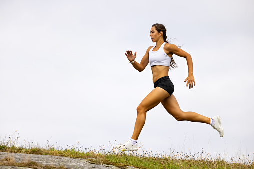 Confident and fit female athlete sprinting on mountain against sky during high intensity interval training
