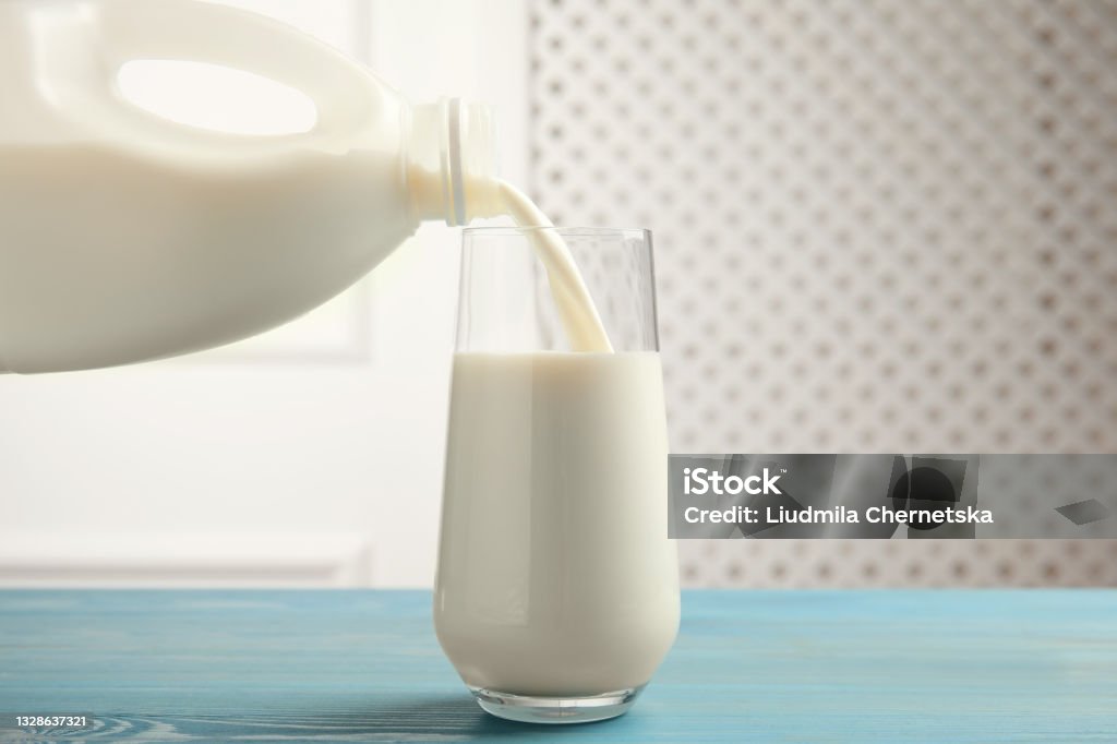 Pouring milk from gallon bottle into glass on blue wooden table Milk Stock Photo