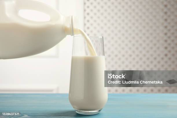 Pouring Milk From Gallon Bottle Into Glass On Blue Wooden Table Stock Photo - Download Image Now