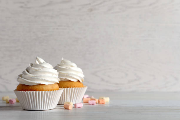 istock Delicious cupcakes with cream and marshmallows on white wooden table. Space for text 1328638183