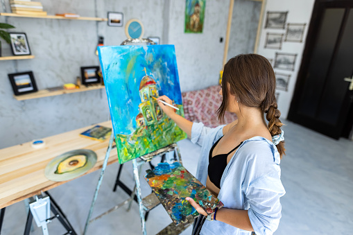 Beautiful young woman painting and drawing in her atelier - art studio