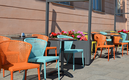 Brightly colored chairs and small tables in a street restaurant are inviting people to sit down