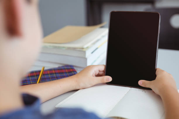 istock Caucasian schoolboy in classroom sitting at desk using tablet, with copy space on screen 1328645384
