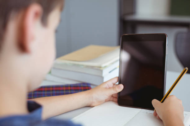 istock Caucasian schoolboy in classroom sitting at desk using tablet, with copy space on screen 1328645485