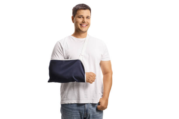 jeune homme au bras cassé portant une attelle de bras et souriant - physical injury men orthopedic equipment isolated on white photos et images de collection