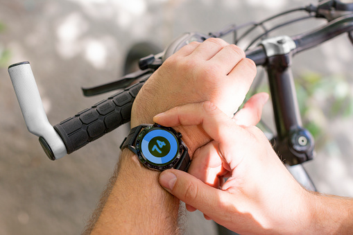 Hands of a man with a smartwatch in close-up while cycling. The concept of modern technologies in sports.