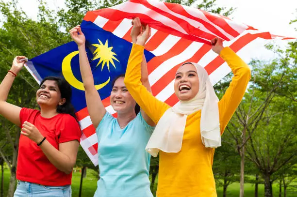 Photo of Three young Malaysians from all races raising a big Malaysian flag and proudly display their patriotic spirit and solidarity in celebrating the Malaysia National Day