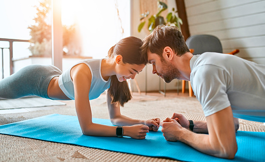 A cute couple in sportswear do an exercise plank on the mats in the living room at home. Healthy lifestyle, sports, yoga, fitness.