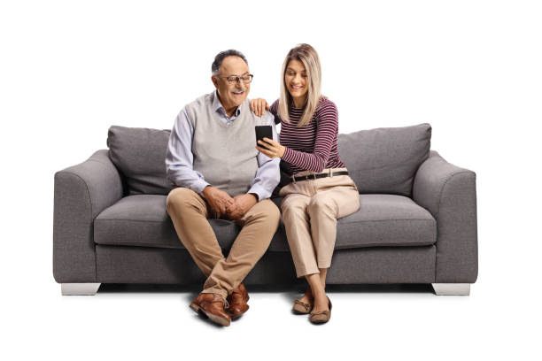 starszy mężczyzna i młoda kobieta siedzą na kanapie i patrzą na telefon komórkowy - family sofa men sitting zdjęcia i obrazy z banku zdjęć