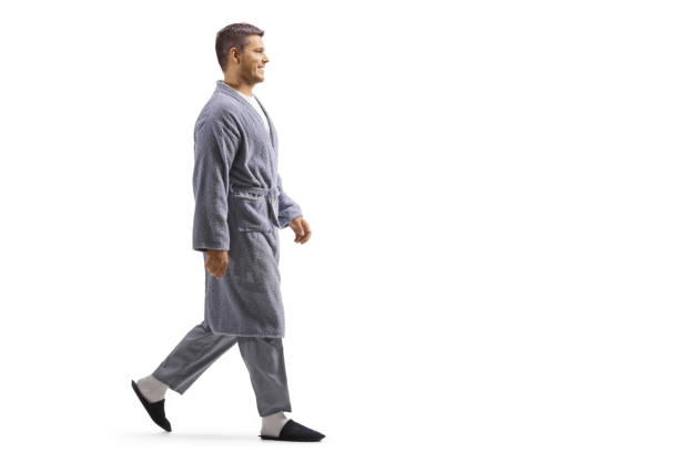 Full length profile shot of a young man wearing a robe and walking Full length profile shot of a young man wearing a robe and walking isolated on white background pajamas stock pictures, royalty-free photos & images