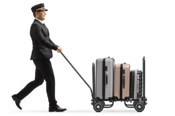 スーツケースでトロリーカートを歩いたり押したりするベル少年の全長プロファイルショット - luggage cart ストックフォトと画像
