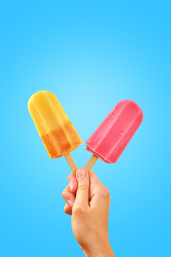 Red and yellow ice creams in woman hand on blue background with copy space. Summer background