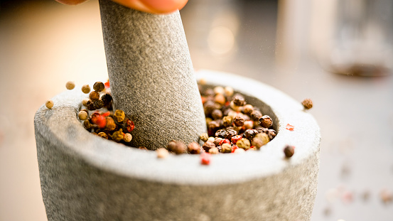 Close-up of different types of peppers being crushed in a mortar with a granite pestle.