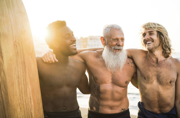istock Multi generational surfer friends having fun on the beach after surf session - Focus on senior man face 1328658009