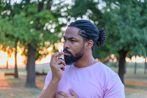 An African-American Man with Breathing Problems is Feeling Displeased and Using a Nasal Spray During a Walk in City Park During a Summer Day.