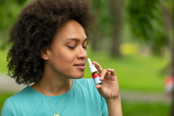 Young African-American Woman with Asthma is Using Inhaler in a Park. A Woman of African-American Ethnicity is Using Nasal Spray Due to the Problems with Nose and Breathing in the Public Park. nasal spray stock pictures, royalty-free photos & images