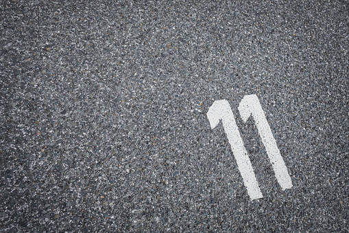 sign on the asphalt, white painted number eleven on grey street, space for text