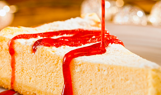 Close-up of pouring red fudge sauce on slice of cake.