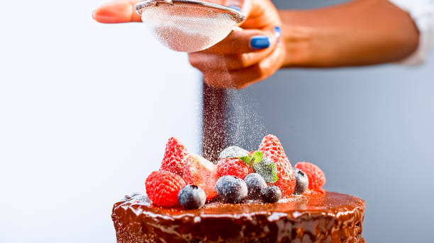 istock Woman dusting caster sugar on chocolate cake 1328664829