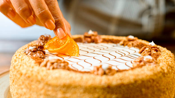 Close-up of woman's hand placing orange slice on top of walnut cake.
